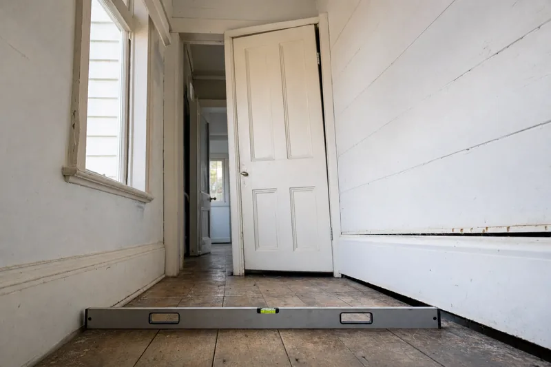 A spirit level lying on a timber floor in a hallway, with a gap along the base of the wall beside it — house levelling, Melbourne. Illustrative example.